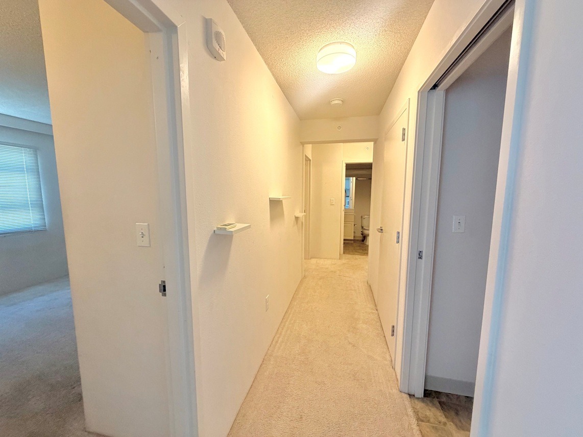 A long, narrow hallway with white walls and carpeted flooring.